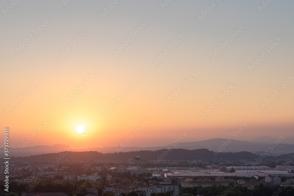 Aerial panoramic sunset view of residential district with buildings of Brescia city and Alps mountain range, blue cloudy sky background, Lombardy, Italy. Brescia Castle.