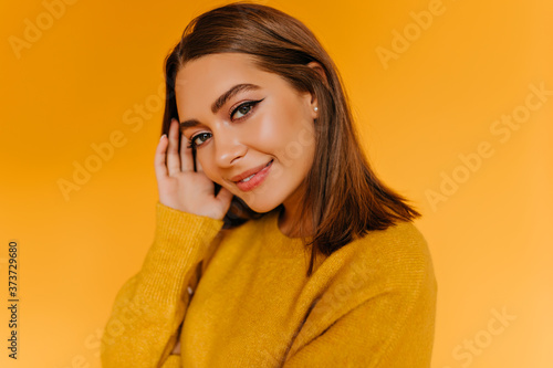 Pleased white woman with trendy makeup posing on orange background. Indoor photo of inspired female model in yellow sweater.