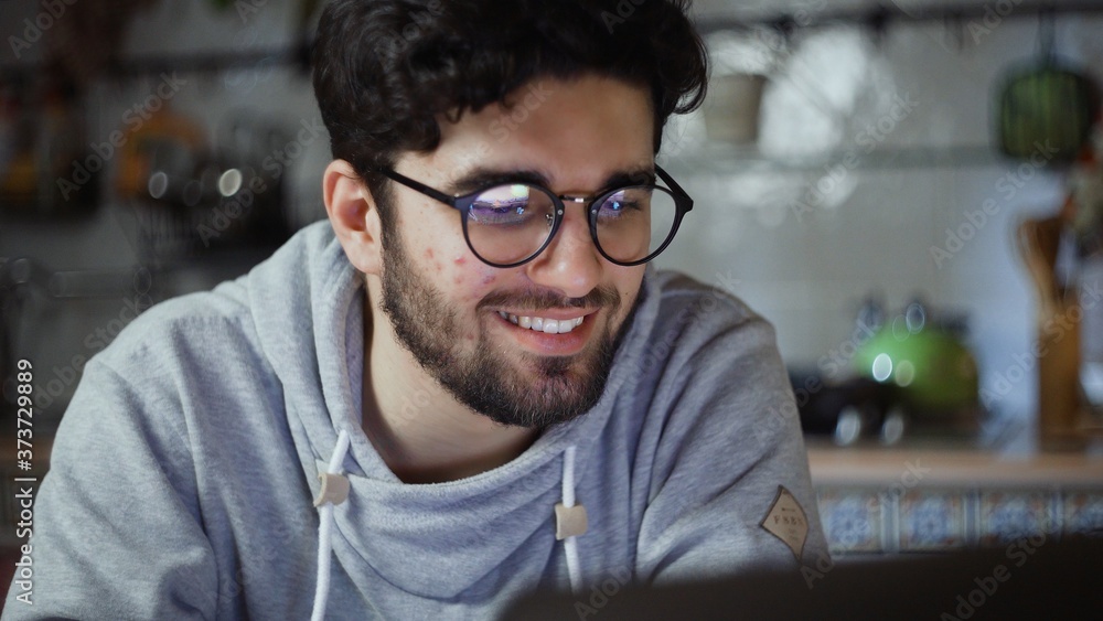 Close up of happy man working on laptop in kitchen at home at night Close up of happy man working on laptop in kitchen at home at night