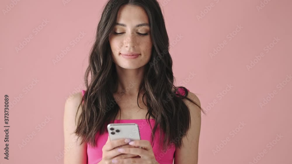 A happy young woman is messaging using her smartphone isolated over a pink background A happy young woman is messaging using her smartphone isolated over a pink background