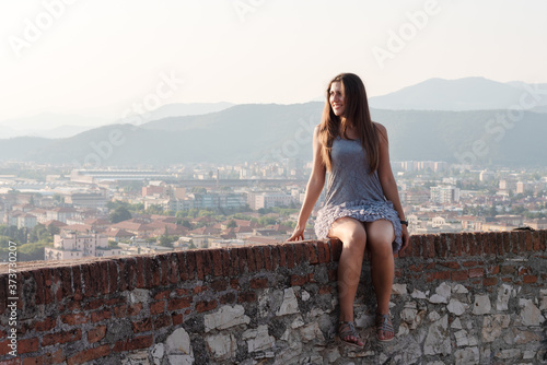 Beautiful girl on the roof terrace with aerial view of the old Italian city Brescia at sunset.
