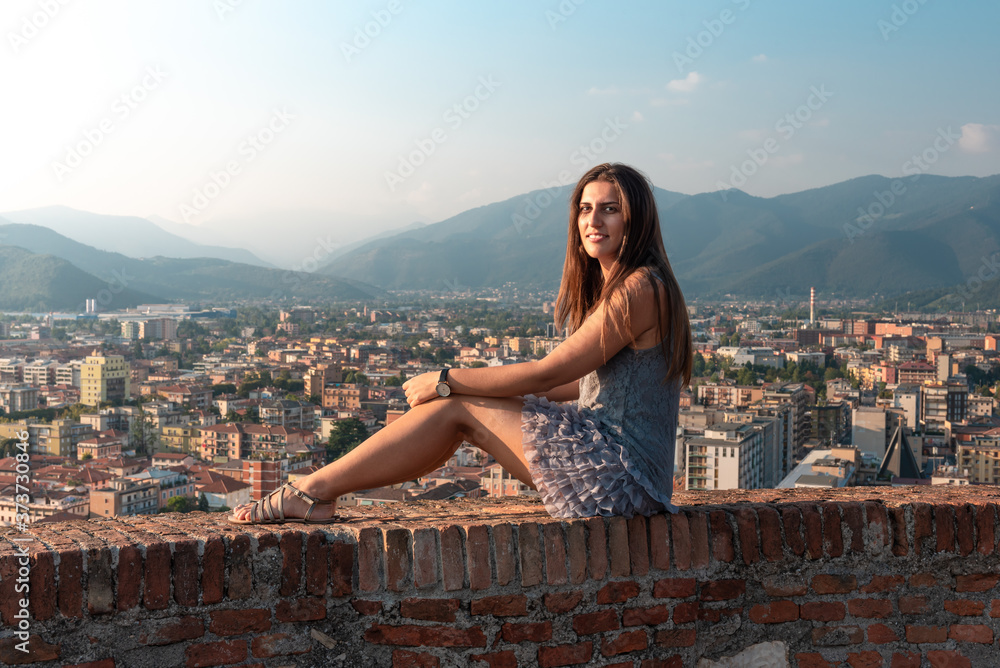Beautiful girl on the roof terrace with aerial view of the old Italian city Brescia at sunset.
