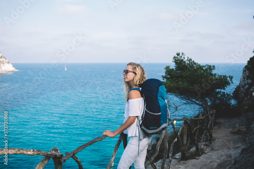 Carefree Caucasian backpacker enjoying scenery landscape views of Menorca looking around during adventure summer journey, female solo traveller with touristic rucksack standing at nature altitude