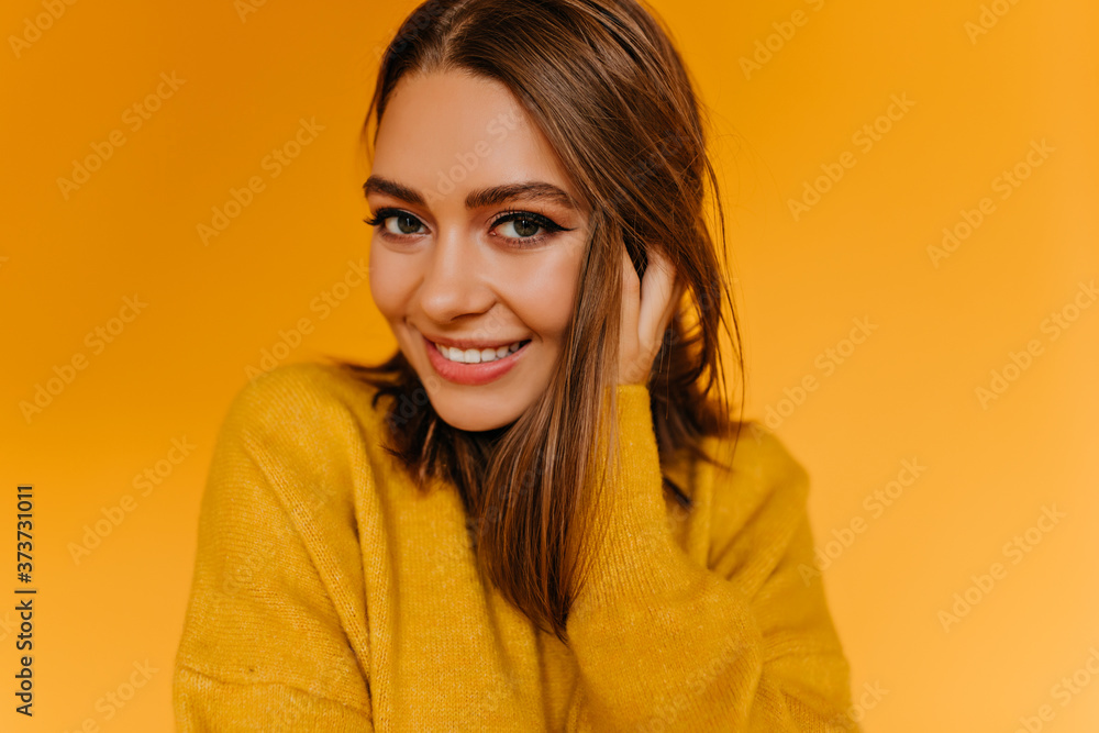 Good-humoured young lady playfully touching her brown hair. Indoor portrait of lovely smiling girl isolated on yellow background. Good-humoured young lady playfully touching her brown hair. Indoor portrait of lovely smiling girl isolated on yellow background.