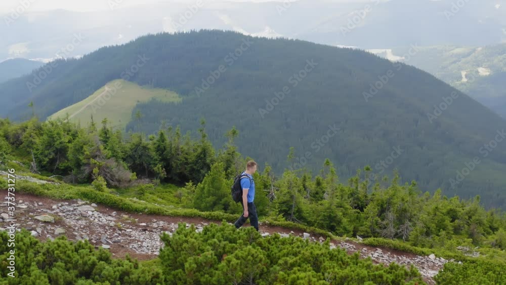 Man backpacker walks along the edge of a mountain peak. Aerial view of male trekking Man backpacker walks along the edge of a mountain peak. Aerial view of male trekking