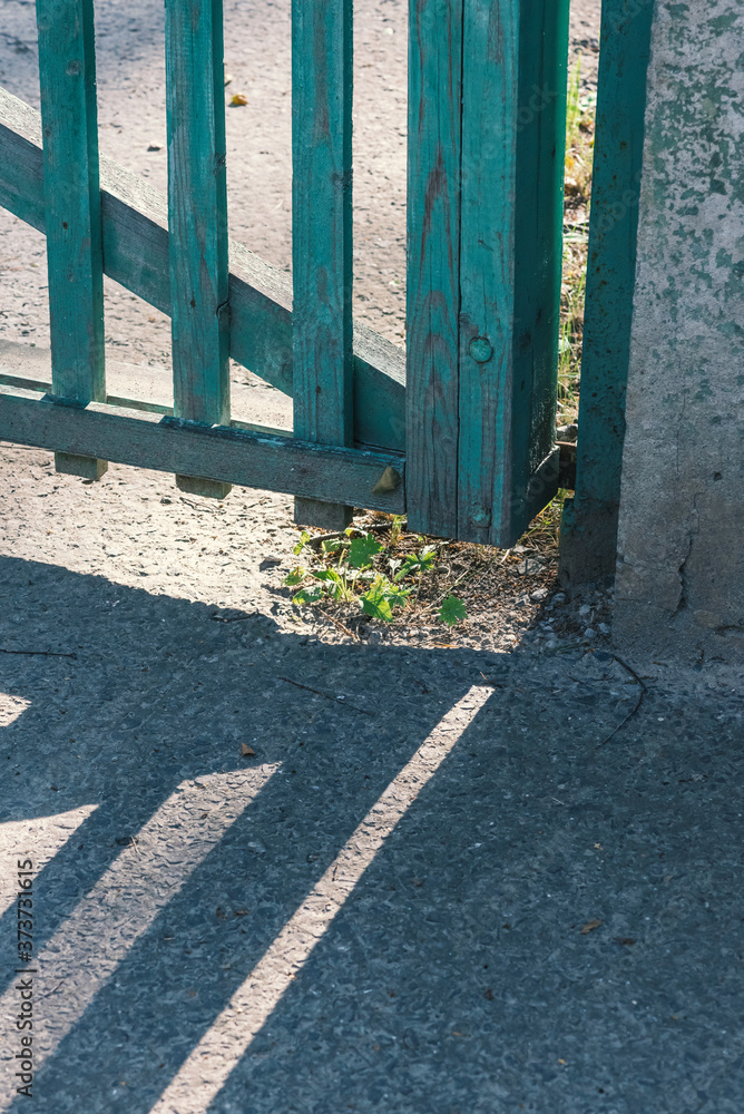 Φωτογραφία Detail of an old green painted wooden fence casting a shadow on a walkway