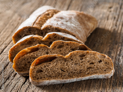 Ciabatta. Dark fresh healthy flattish open-textured Italian bread with a floury crust made with olive oil on wooden background. Close-up