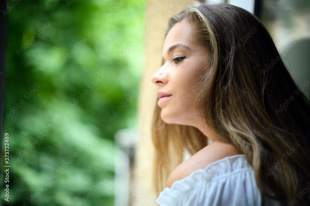 Young woman looking through a window at home Young woman looking through a window at home