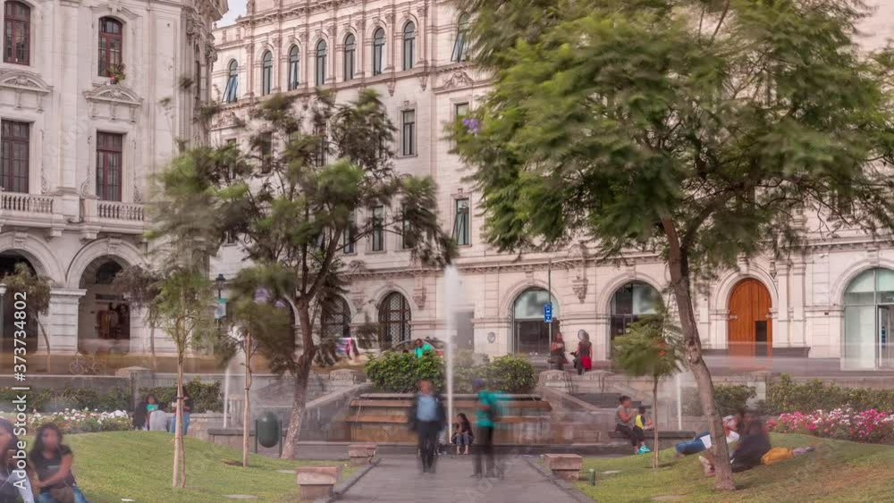 Fountain on Plaza San Martin in the city of Lima with several people are resting near timelapse. Green lawn and trees. Historic buildings on a background