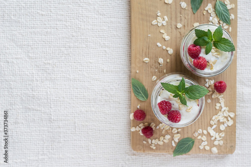 Two portions of homemade natural yogurt with oats and fresh raspberries in glass jars on a light background. Top view, copyspase