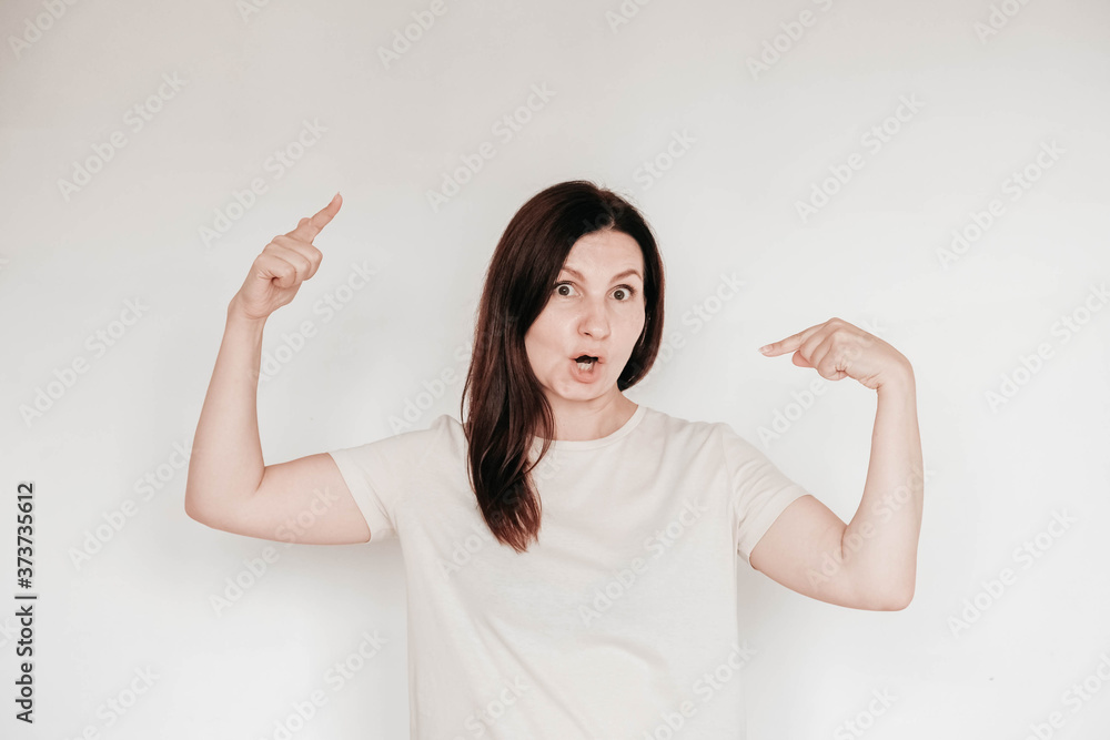 Emotional brunette woman with surprised face keeps holds hands in near the head, dressed in casual white t shirt, poses indoor on a white background. Copy, empty space for text Emotional brunette woman with surprised face keeps holds hands in near the head, dressed in casual white t shirt, poses indoor on a white background. Copy, empty space for text