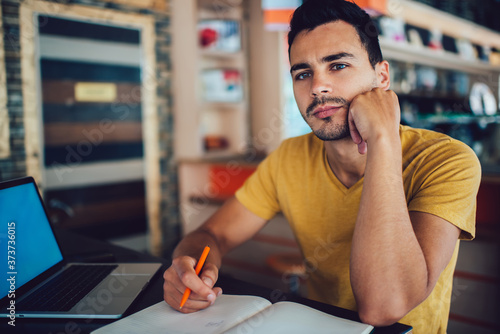 Thoughtful young male student writing essay in cafe photo