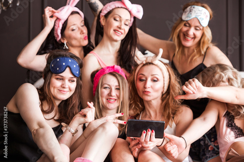Many girlfriends girls threw a pajama party on a plush bed. Girls smile, look at the camera and take a selfie