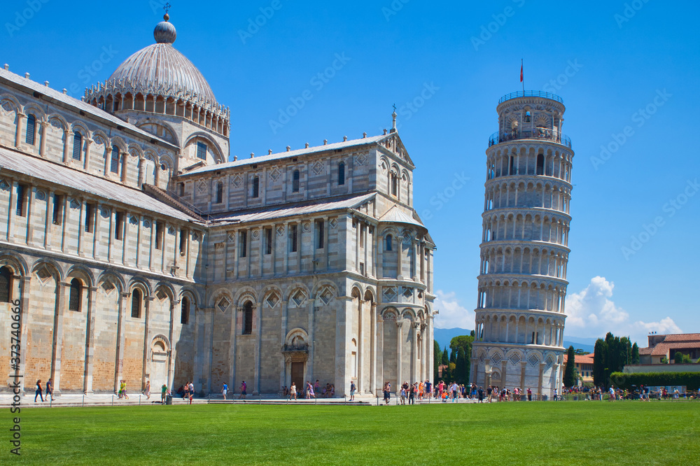 leaning pisa tower and baptistery with meadow and blue sky
