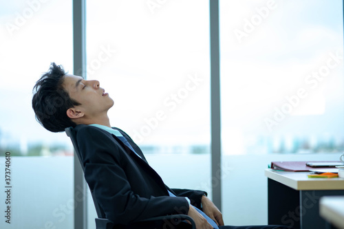 Businessman sitting at workplace near feeling Tired exhaustion and tiredness after long hard working day, overwork and stressful work.