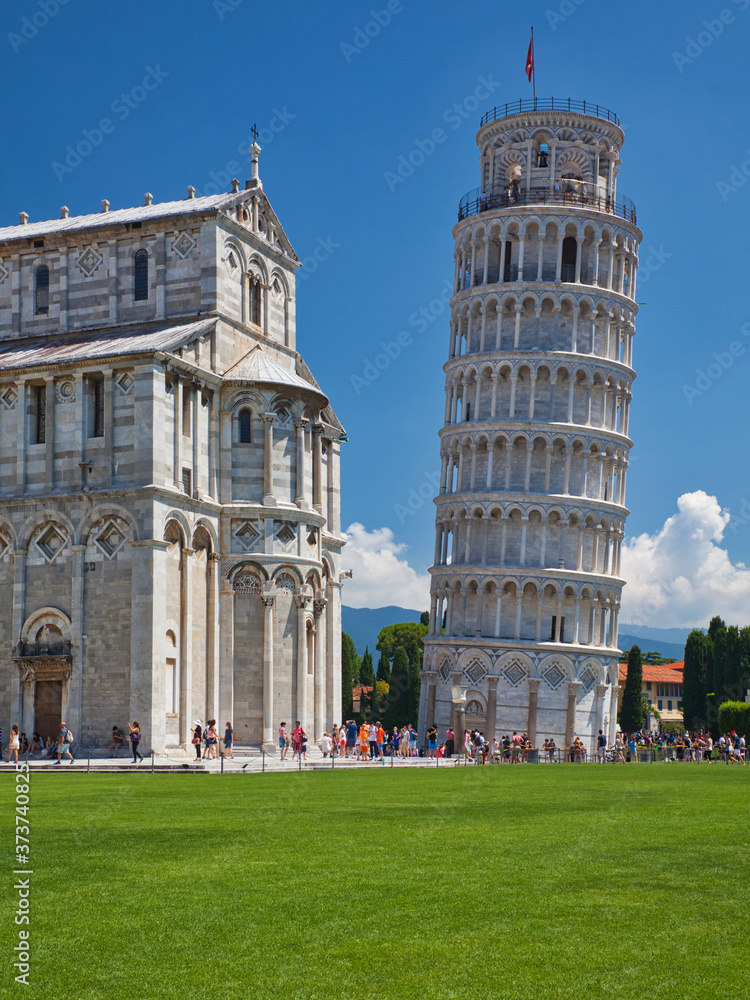 leaning pisa tower and baptistery with meadow and blue sky