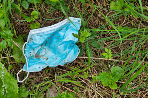 A used, blue surgical mask used for COVID-19 protection, discarded as litter in rural countryside causing environmental pollution
