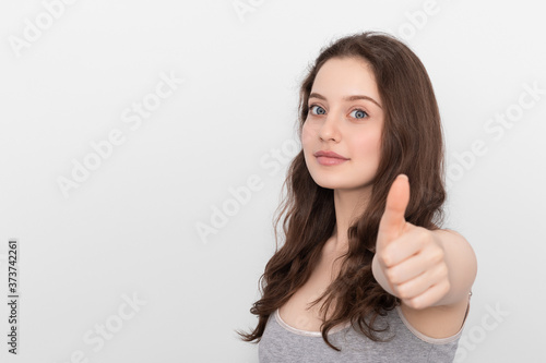 Girl shows thumbs up to the camera, focus on the girl. Young girl with long hair and blue eyes. Copy space. © Snizhana