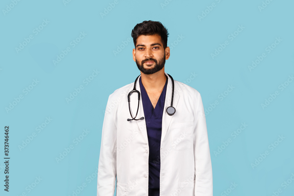 Handsome modern Indian / Asian doctor with stethoscope, in uniform on blue background Handsome modern Indian / Asian doctor with stethoscope, in uniform on blue background