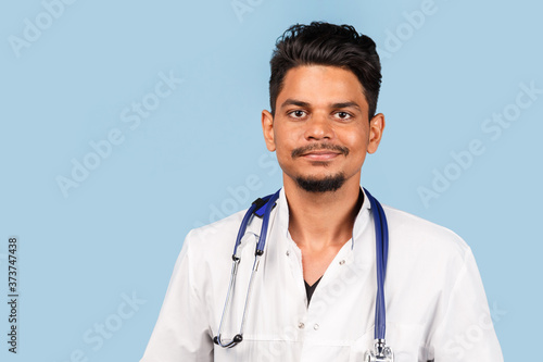 Handsome modern Indian / Asian doctor with stethoscope, in uniform on blue background