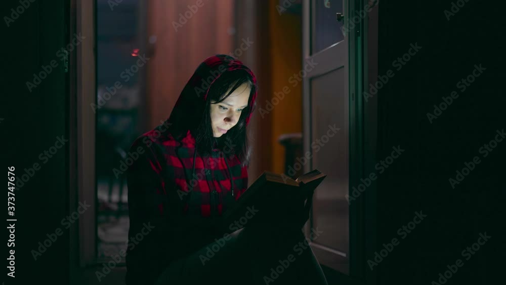 Young woman sitting on porch and reading book at night. Adult female resting with book on fresh air, enjoying her leisure time. Young woman sitting on porch and reading book at night. Adult female resting with book on fresh air, enjoying her leisure time.