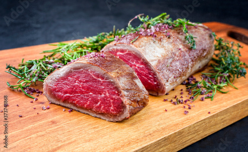 Gebratenes dry aged Angus Filet Steak vom Rind  natur mit Kräuter und Rotwein Salz angeboten als close-up auf einem Modern Design Holz Board