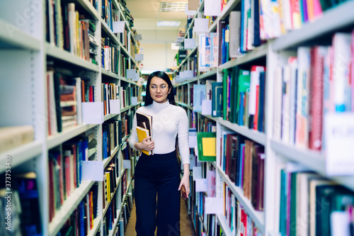 Asian woman walking between bookcases in library