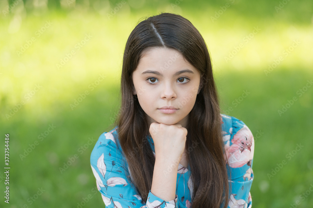 Little girl with long hair relaxing in park sunny day green grass background, sad thoughts concept Little girl with long hair relaxing in park sunny day green grass background, sad thoughts concept