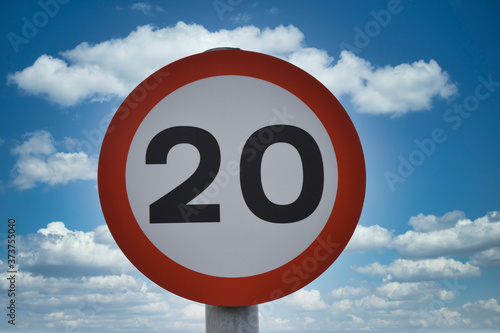Twenty miles per hour speed limit sign, isolated against blue sky and white clouds background. Taken in UK.