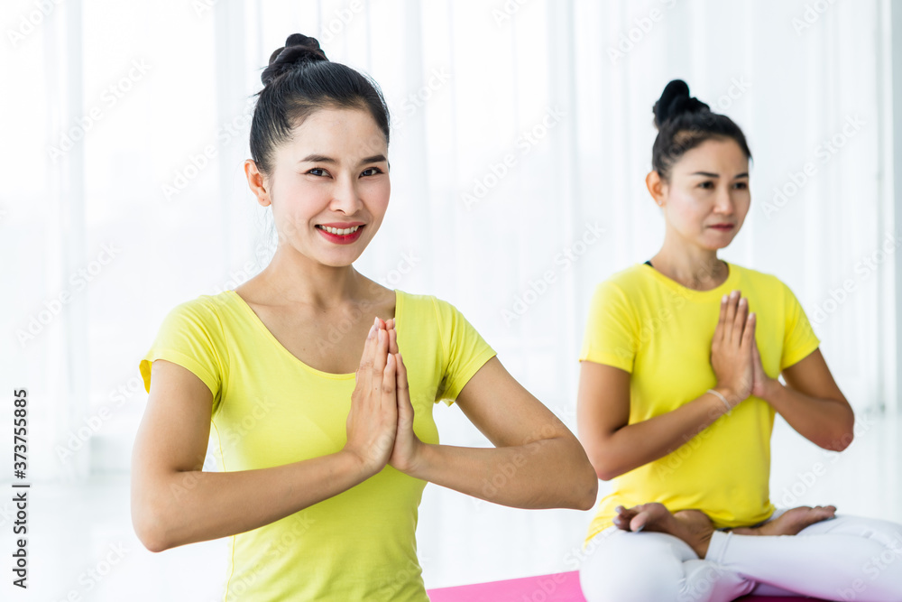 Two young Asian women workout practicing yoga in yellow dress or pose with a trainer and practice meditation wellness lifestyle and health fitness concept in a gym. Two young Asian women workout practicing yoga in yellow dress or pose with a trainer and practice meditation wellness lifestyle and health fitness concept in a gym.