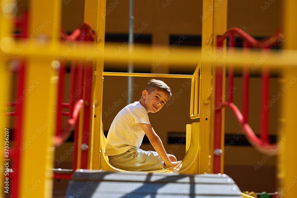Obraz premium Seven-year-old boy rides a yellow slide in the playground