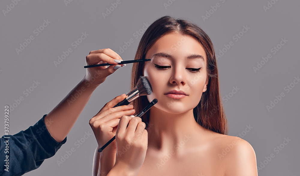 Cute attractive girl with makeup brushes isolated on gray background. Beauty salon, make-up. Cute attractive girl with makeup brushes isolated on gray background. Beauty salon, make-up.