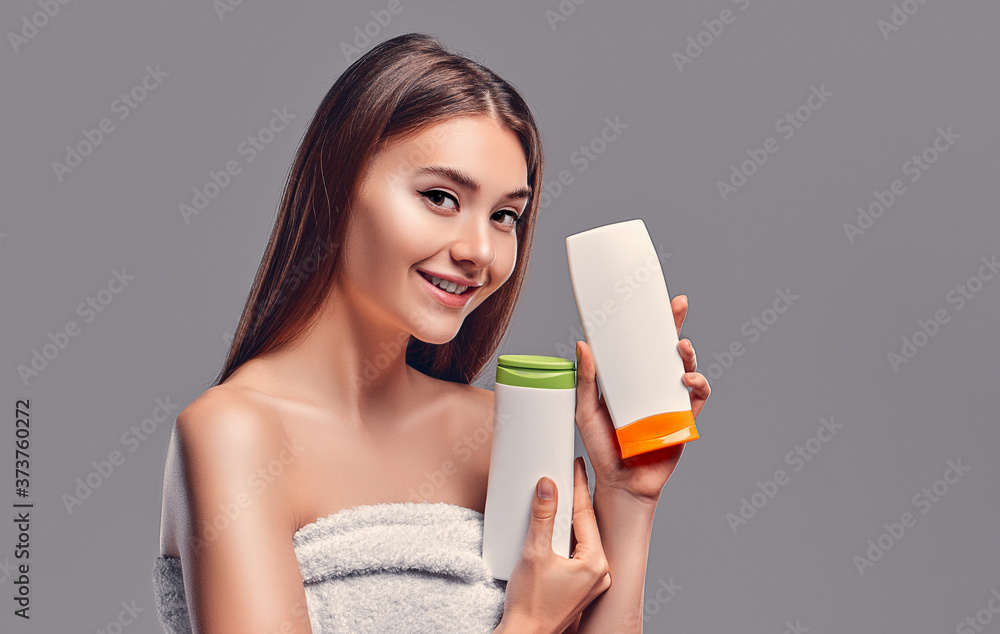 Portrait of attractive young woman with two shampoos on grey background. Making choice. Women care Portrait of attractive young woman with two shampoos on grey background. Making choice. Women care
