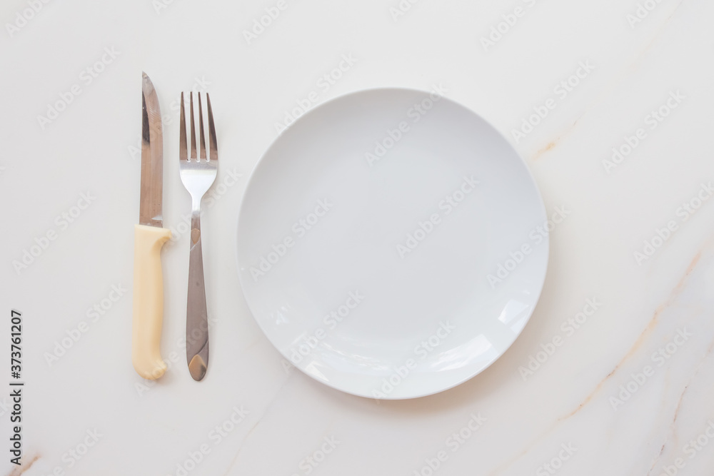 Empty white plate with cutlery on a marble table, saucer, fork and knife. The concept of diet, fasting Empty white plate with cutlery on a marble table, saucer, fork and knife. The concept of diet, fasting