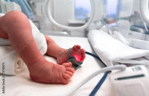 Premature baby feet with a neonatal pulse oximetry monitor, selective focus. Small newborn is placed in a premature newborn incubator. Neonatal intensive care unit