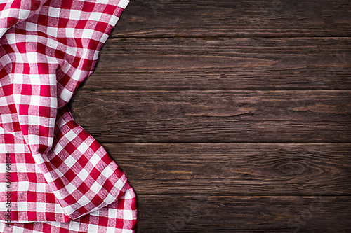 Red and white checkered fabric table cloth on brown wooden planks table background,copy space, top view.Restaurant wallpaper banner background for menus, food photos, cafes...