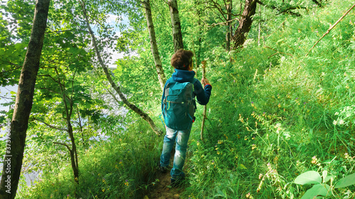 A boy with a headlamp walks along a hiking route according to an orienteering assignment in the forest around a mountain lake. Boy traveler with tourist equipment goes to the family camping.