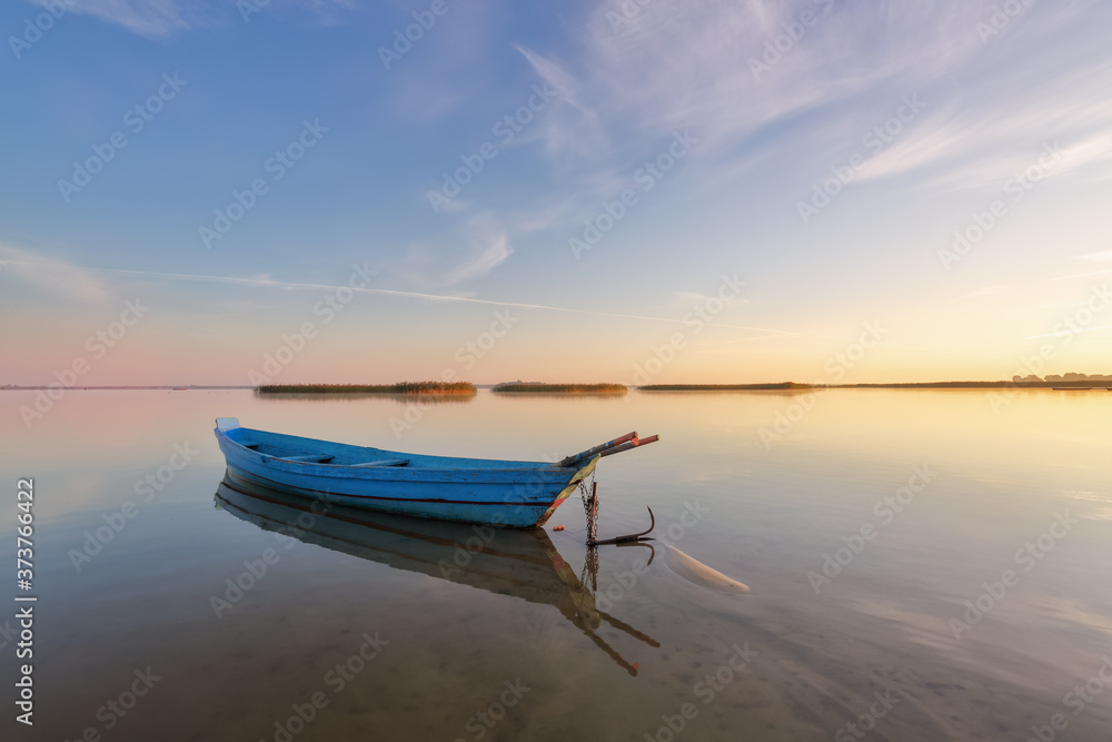 Lonely boat in calm lake. The silhouette is reflecting on the water. Beautiful summer day. Amazing sunrise. Blue sky with clouds. Location place Svityaz lake, Ukraine, Europe.