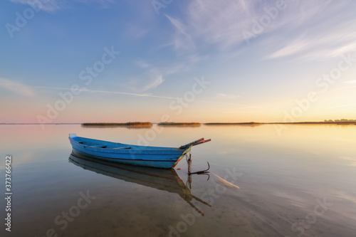 Lonely boat in calm lake. The silhouette is reflecting on the water. Beautiful summer day. Amazing sunrise. Blue sky with clouds. Location place Svityaz lake, Ukraine, Europe.