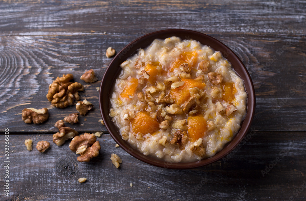 Delicious oatmeal porridge with baked pumpkin, honey and nuts in ceramic bowl on wooden table. healthy homemade breakfast. selective focus