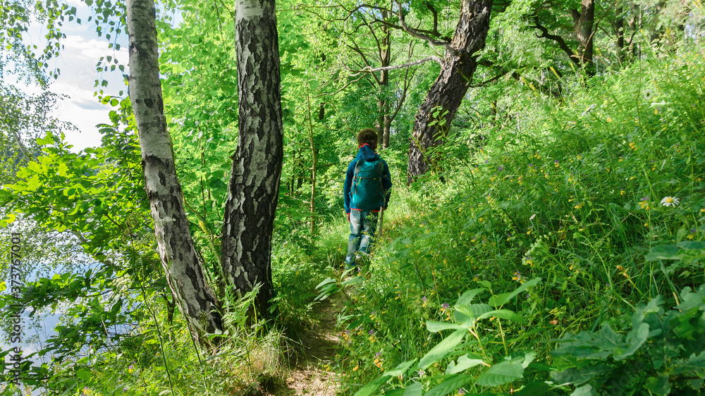 Survival techniques in the forest for children. A boy with camping equipment walks on a hiking trail in a temperate forest. Sport orienteering for children. Survival techniques in the forest for children. A boy with camping equipment walks on a hiking trail in a temperate forest. Sport orienteering for children.
