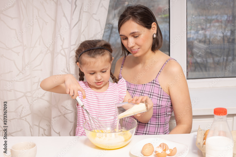 A little cute girl and her mother preparing the dough in the kitchen at home, happy family concept A little cute girl and her mother preparing the dough in the kitchen at home, happy family concept