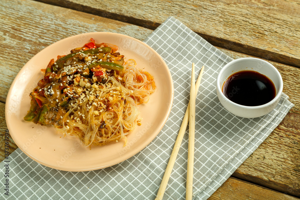 Funchoza with vegetables and mushrooms in a plate on a napkin near sticks and soy sauce. Funchoza with vegetables and mushrooms in a plate on a napkin near sticks and soy sauce.