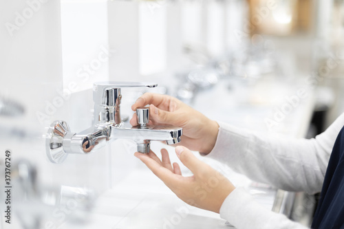 Foto Pretty young woman choosing a bathroom/kitchen tap in a home furnishings retail