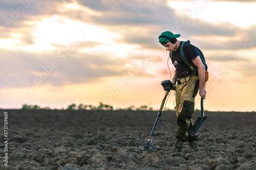 Treasure hunter with metal detector in a field at sunset