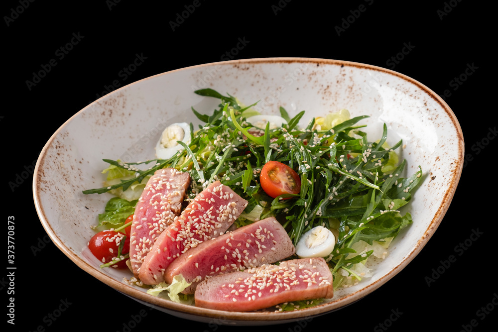 Salad with sliced steak of tuna in sesame, arugula, tomatoes and quail eggs. Tuna salad isolated on black. Salad with sliced steak of tuna in sesame, arugula, tomatoes and quail eggs. Tuna salad isolated on black.