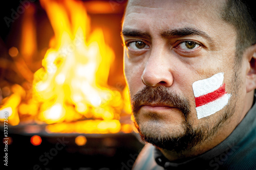 Man with a painted a white and red flag of the revolution on his face. Protest against the dictatorial regime in Belarus and falsification of presidential elections. People strike. Fire background photo