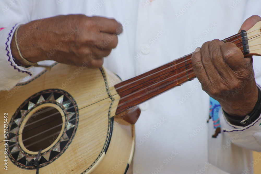 hands of a man playing a wooden guitar with white clothes and Mexican decorations