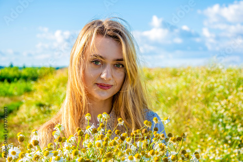 portrait of a beautiful smiling girl with hair fluttering in the wind with a large bouquet of wildflowers against the background of a blue sky and a green field. minimum of makeup. unity with nature.