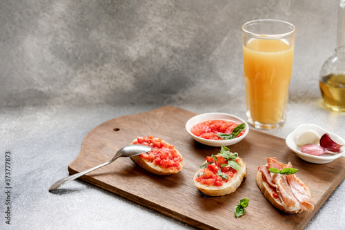 bruschetta, toast, with sliced tomatoes, jamon and Basil on a wooden cutting Board and orange juice in a glass Cup. copy space